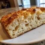 Close-up of a slice showing the airy, open crumb structure of garlic parmesan focaccia bread recipe.