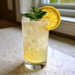 A tall glass filled with crushed ice and a yellow ginger lemon cooler, garnished with fresh mint and a lemon slice.