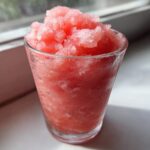 Close-up of a glass filled with icy, bright pink frozen strawberry lemonade.