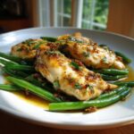 Close-up of glazed chicken breasts served over bright green beans, featuring a savory sauce and fresh parsley.