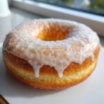 Close-up of a fluffy, golden-brown glazed cottage cheese donut dripping with white icing.