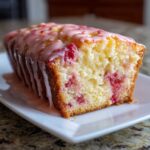 A moist slice of homemade strawberry bread topped with a thick, pink strawberry glaze dripping down the sides.