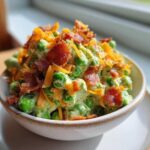 A creamy bowl of green pea salad with bacon and cheese topping, photographed in natural light.