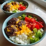 Close-up of a high protein burger bowl featuring seasoned burger patties, cauliflower rice, melted cheese, lettuce, tomatoes, and pickles.