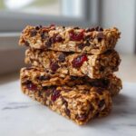 A close-up stack of three chewy homemade granola bars packed with oats, chocolate chips, and dried cranberries.