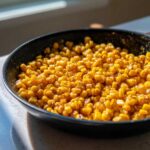 Close-up of glossy, golden kernels of honey butter skillet corn cooking in a black skillet.