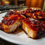 Close-up of juicy bbq chicken breast sliced open, showing moist white meat covered in a thick, glossy BBQ sauce glaze.