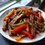 Close-up of perfectly cooked steak fajita strips mixed with vibrant red, orange, and green bell peppers and onions.