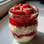 Close-up of layered cottage cheese strawberry cheesecake chia seed pudding in a glass jar, topped with fresh strawberries.