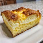 A close-up of a square slice of lemon cream cheese dump cake showing a fluffy yellow cake base and a thick, creamy white filling.