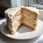 A tall, three-layer London fog cake recipe with white frosting, a slice removed to show the fluffy interior.