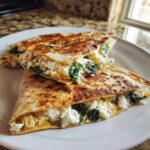 Two halves of a golden-brown mediterranean quesadillas filled with white cheese (feta) and wilted spinach.