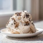 A scoop of light, airy meringue topping sprinkled with chocolate chips, resembling forgotten cookies.