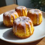 Four bright yellow mini lemon cakes with lavender glaze drizzled over the top, garnished with dried lavender buds.