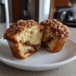 A cinnamon muffin cut in half showing the moist interior, cinnamon swirl, and crunchy streusel topping.