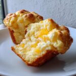 Close-up of a moist pineapple muffin broken in half, showing chunks of bright yellow pineapple inside the crumb.