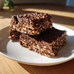 Two stacked squares of rich no bake chocolate oatmeal bars showing the texture of oats bound by chocolate.
