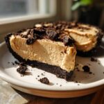 A close-up of a thick slice of no bake peanut butter pie with a dark chocolate crust and cookie topping.