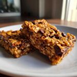 Two rich, chewy oatmeal chocolate chip peanut butter bars studded with chocolate chips, resting on a white plate.