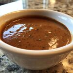 Close-up of rich, brown swedish meatball sauce seasoned with herbs in a small white bowl.