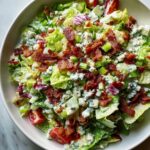 A vibrant bowl of ruths chris chopped salad featuring crisp lettuce, blue cheese crumbles, celery, and crispy bacon pieces.