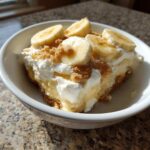 A delicious serving of banana pudding topped with whipped cream, sliced bananas, and graham cracker crumbs.