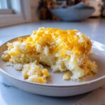 A close-up serving of creamy hashbrown casserole topped with melted cheddar cheese.