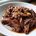 Close-up of juicy, shredded Mississippi Pot Roast served in a white bowl with visible pepperoncini slices.