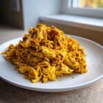 A mound of vibrant yellow, shredded slow cooker chicken shawarma piled high on a white plate.