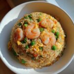 A perfectly molded serving of shrimp fried rice recipe featuring plump shrimp, green peas, and scrambled egg in a white bowl.