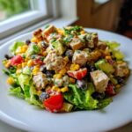 Close-up of a vibrant spicy southwest salad featuring grilled chicken, corn, black beans, avocado, and tomatoes on lettuce.