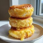 A stack of three fluffy, golden lemon rolls generously topped with thick, dripping lemon glaze.