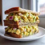 A tall, stacked sandwich filled generously with creamy easy chickpea salad, red onion, and celery on whole wheat bread.