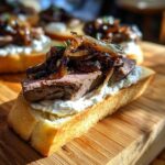 Close-up of a single steak crostini topped with creamy cheese, medium-rare steak, and caramelized onions.