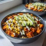 A vibrant sweet potato taco bowl recipe featuring roasted sweet potatoes, black beans, corn, avocado slices, and a creamy white drizzle.