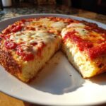 Close-up of a thick, golden-brown cottage cheese pizza crust, sliced open to show the texture, topped with sauce and melted cheese.