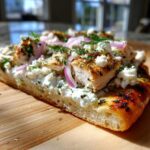 Cross-section view of a slice of tzatziki chicken naan pizza showing thick crust, creamy tzatziki base, grilled chicken, feta, and red onion.