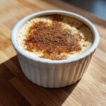 A single serving of creamy vanilla baked custard in a white ramekin, topped with sprinkled cinnamon.
