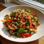 A vibrant Thai chicken salad recipe featuring shredded chicken, carrots, red peppers, mint, and crushed peanuts in a white bowl.