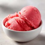 Two scoops of bright pink, icy watermelon sorbet served in a small white bowl.