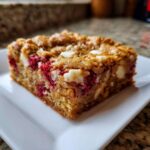 A single, thick square of white chocolate raspberry blondies showing bright red fruit and white chocolate chunks.